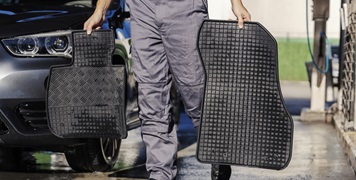 Cropped picture of car wash serviceman carrying car mats at carwash station