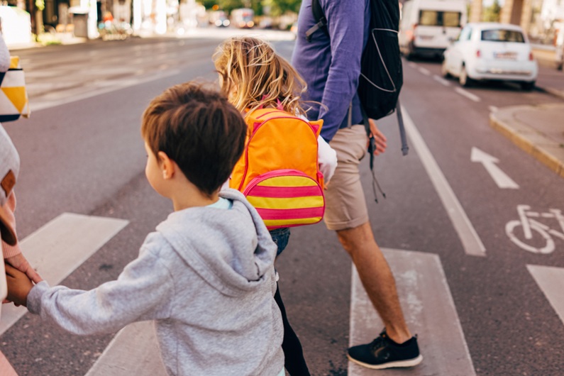 Children holding adult hands while crossing the road at a pedestrian crossing