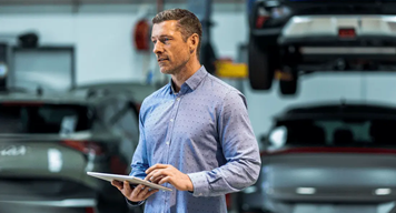 Fleet manager using a tablet in an automotive workshop with cars and a vehicle lift in the background