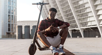 Person sitting on parked eScooter in a city setting