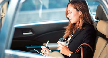 Woman in backseat of car with coffee and a tablet