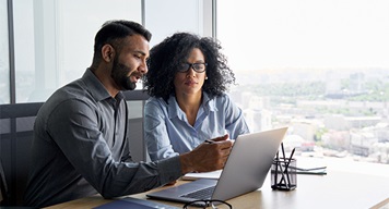 Two colleagues reviewing information on a laptop