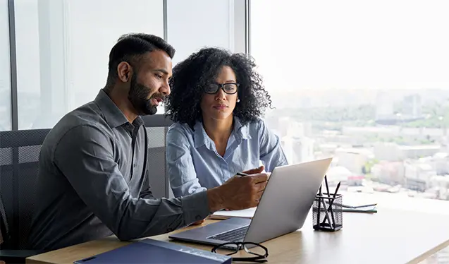 Two colleagues reviewing information on a laptop