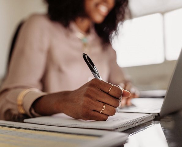 female-holding-pen-to-paper-sitting-in-front-of-laptop