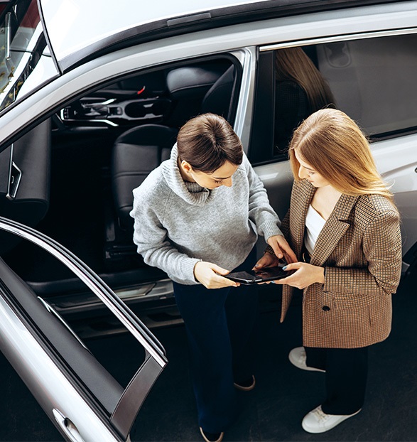 females-looking-at-tablet-next-to-vehicle-in-showroom