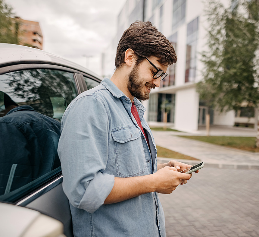 man-smiling-at-phone-next-to-car
