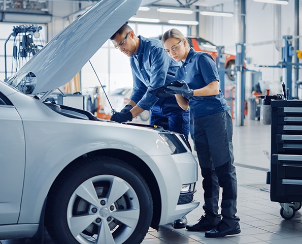 Two Mechanics in a Service are Inspecting a Car After They Got the Diagnostics Results. two-mechanics-in-a-service-inspecting-car-after-diagnostic