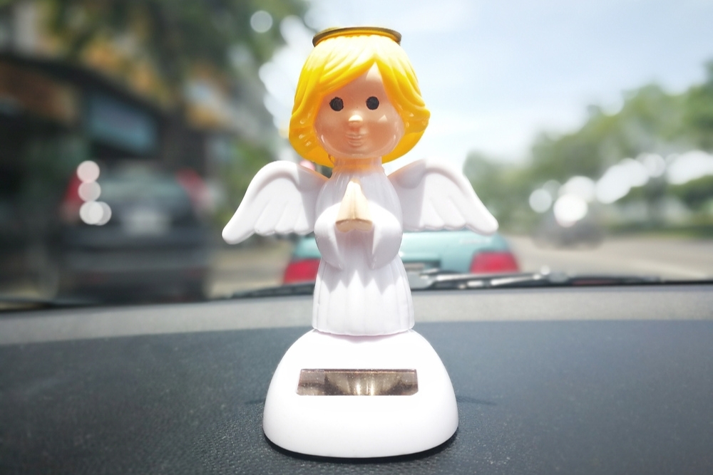 Solar-powered dashboard ornament in the shape of a praying angel, positioned on a car dashboard.