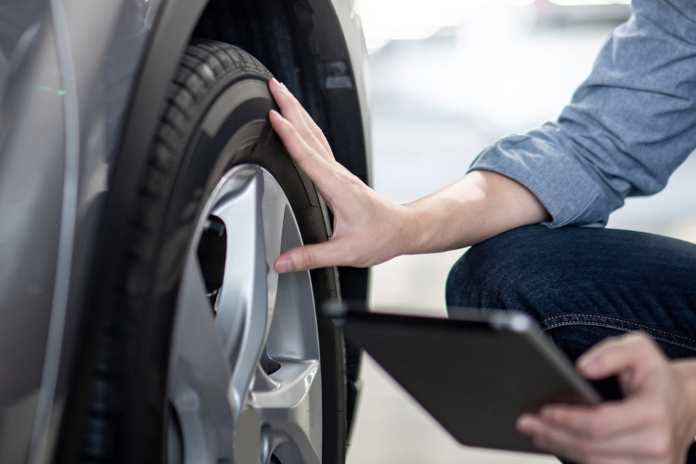 Person inspecting an EV tyre while holding a tablet, suggesting digital vehicle maintenance or pre-drive checks.