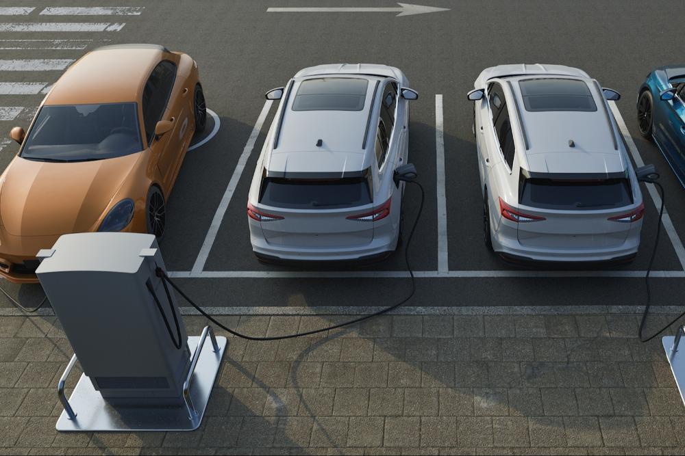 EV production UK An aerial view of electric vehicles parked in charging bays, connected to charging points via cables.