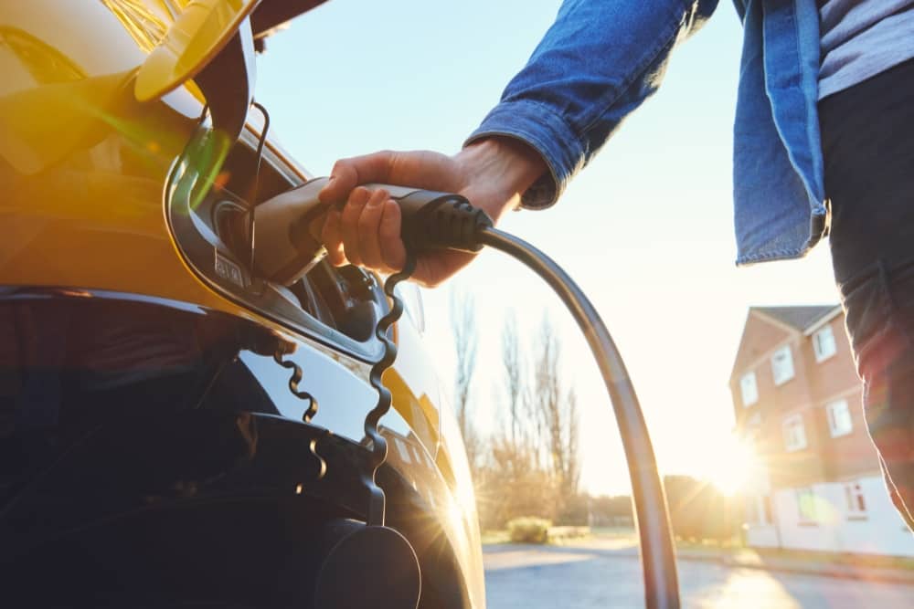 Person plugging in an EV at home, representing the convenience of an EV home charger and the affordability of an EV salary sacrifice scheme as part of employee car benefits.