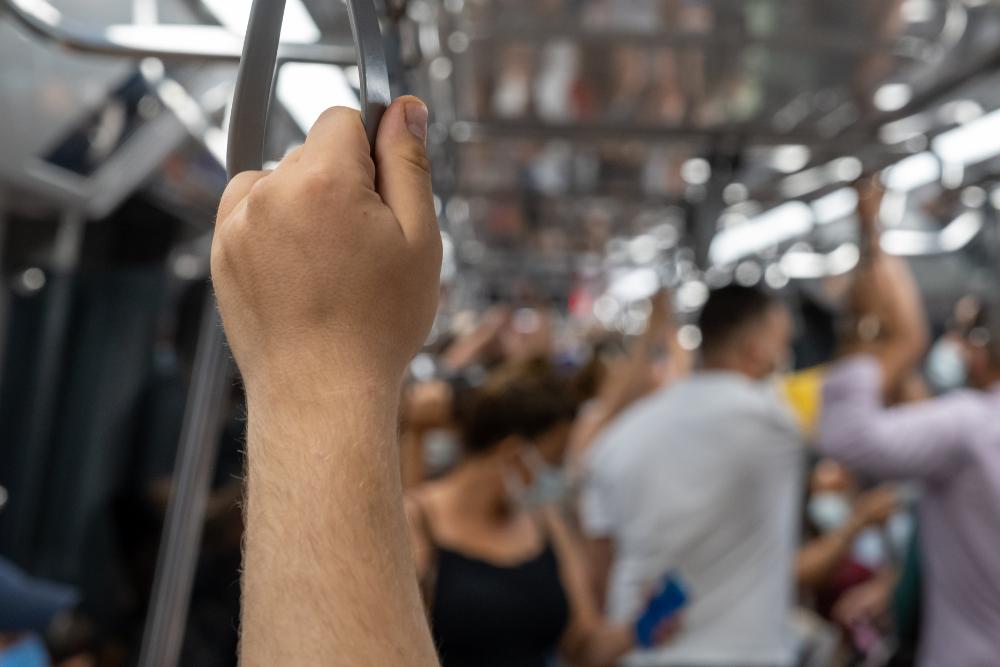 How to stay cool in a car in hot weather in the UK Close-up of a hand gripping an overhead handrail on a crowded train or tube carriage.