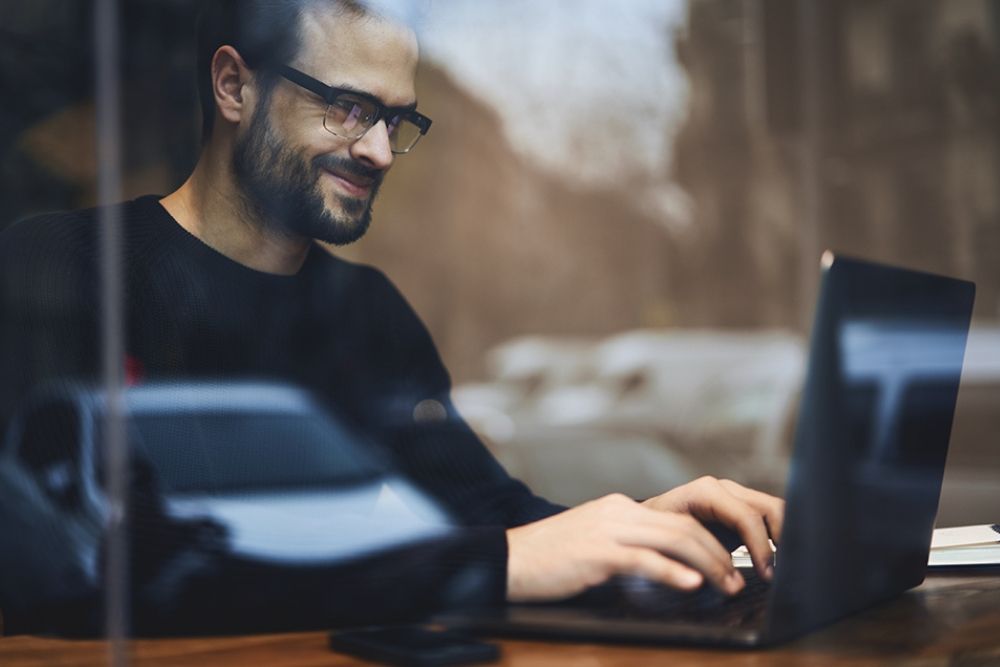 man scaling his fleet growing business Man smiling while working on a laptop in a café, representing strategic planning or digital management of a growing business fleet.