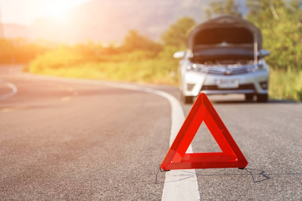 Broken down second-hand car on the roadside with a warning triangle, reflecting poor car service history and reduced car value.