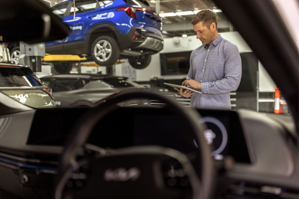 Semiconductor fleet management maintenance An automotive technician in a workshop holds a tablet and inspects multiple cars elevated on hydraulic lifts, showcasing semiconductor-enabled fleet management and maintenance.